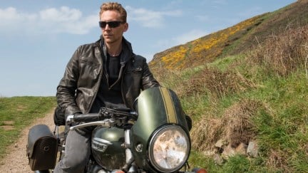 Tom Hiddleston as Jonathan Pine, sitting on a motorcycle wearing a leather jacket.