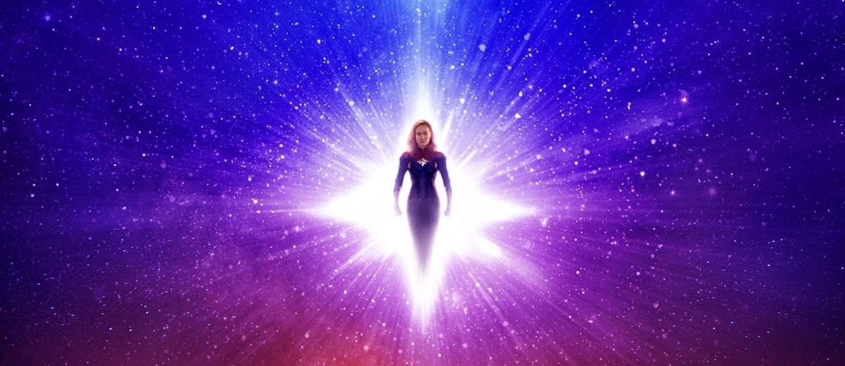Captain Marvel floats in a diamond-shaped portal of light, surrounded by a purple and blue starry sky.
