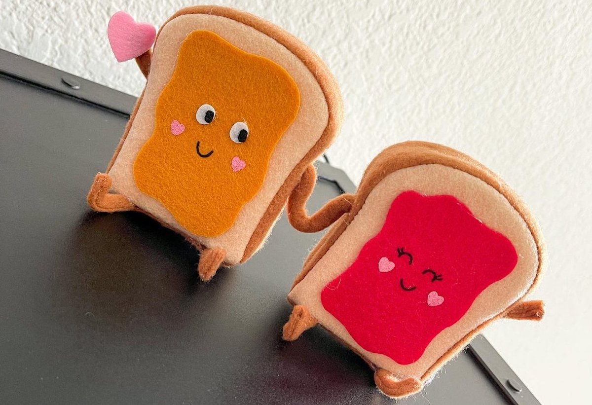 Anthropomorphic slices of bread spread with peanut butter and jam, holding hands and one holding a small pink heart