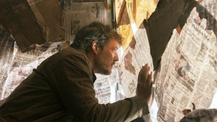 Pedro Pascal's Joel looks out of a window covered in newspapers in 'The Last of Us'
