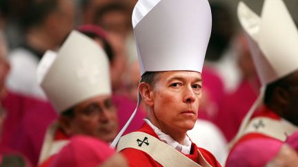 An archbishop in a big pointy white hat stares menacingly at the camera.