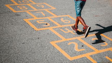 A child is seen from the waist down playing hopscotch.