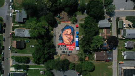 In an aerial view from a drone, a large-scale ground mural depicting Breonna Taylor with the text 'Black Lives Matter' is seen.