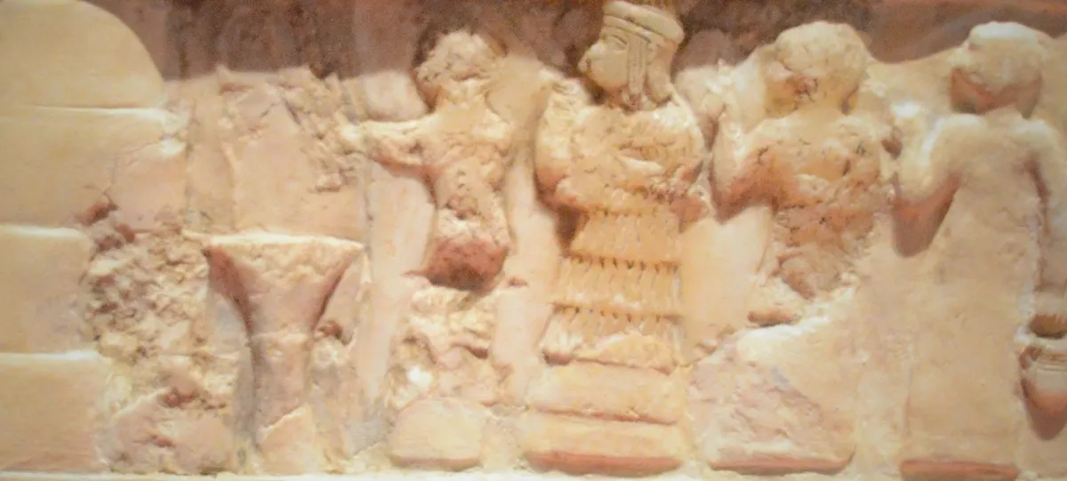 A row of alabaster figures, with a figure in a tiered skirt in the middle. Detail from the Disk of Enheduanna.