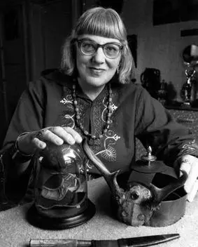 Doreen Valiente, wearing cat eye glasses, sits at a table with various occult tools in front of her.