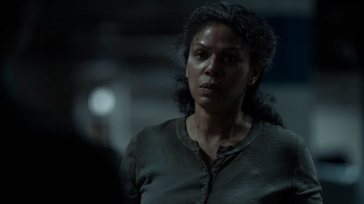 Image of Merle Dandridge as Marlene in HBO's 'The Last of Us.' We see her from the chest up as she stands in a parking garage. Her curly, black hair is in a ponytail, and she's wearing a grey, long-sleeved long-johns-type sweatshirt. She's looking seriously at someone standing in front of her. 