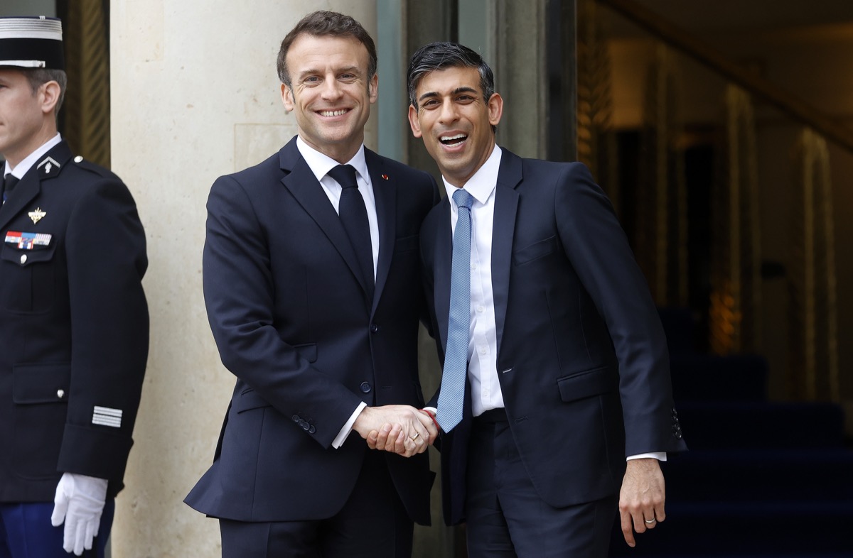 French President Emmanuel Macron welcomes British Prime Minister Rishi Sunak smile widely as they meet to discuss the future of refugee policies