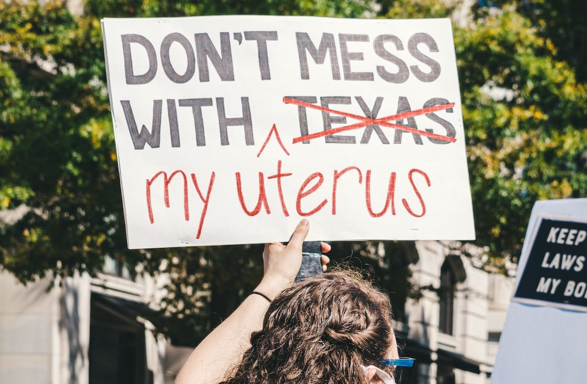 Woman at Texas abortion ban protest with a sign that reads "Don't mess with [Texas] my uterus" with Texas crossed out