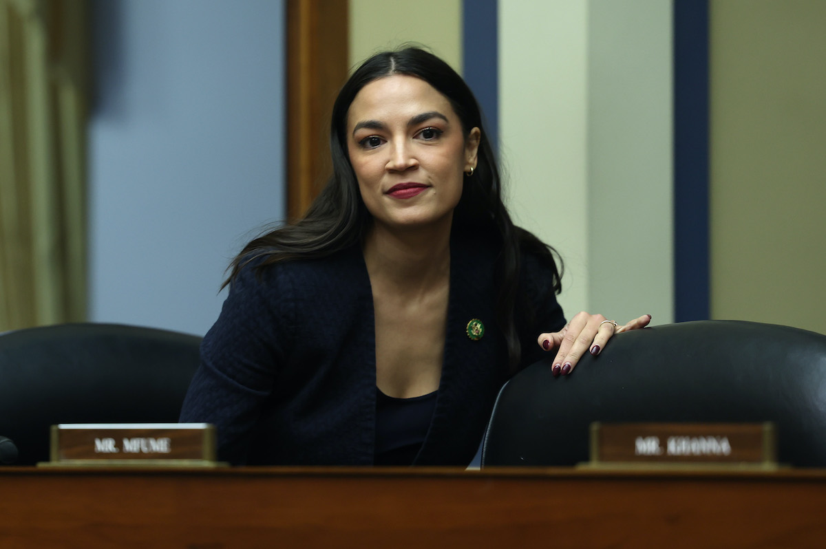 Alexandria Ocasio-Cortez smiles standing behind a desk in the House.