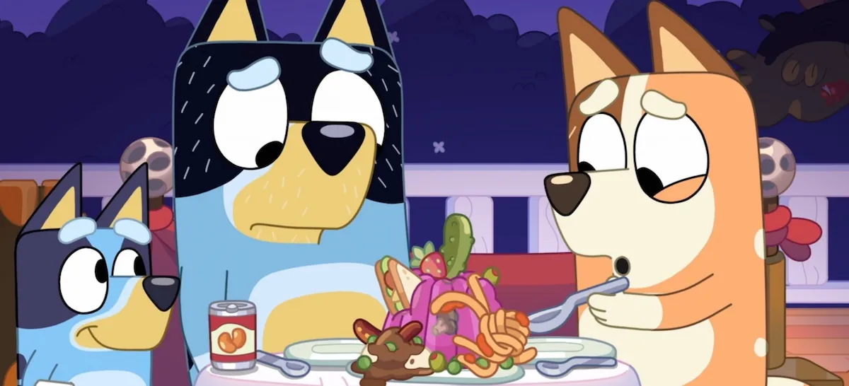 Bandit and Chilli sit at a table, staring in dismay at a disgusting mix of jello and pasta. Bluey stands next to them, smiling.
