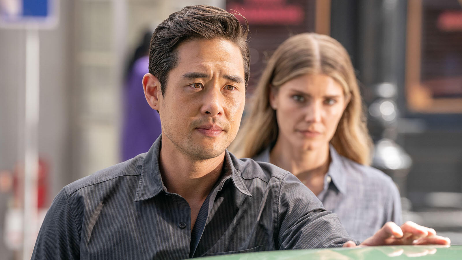 Ben Song looks pensively off camera with Addison looking at him in the background.