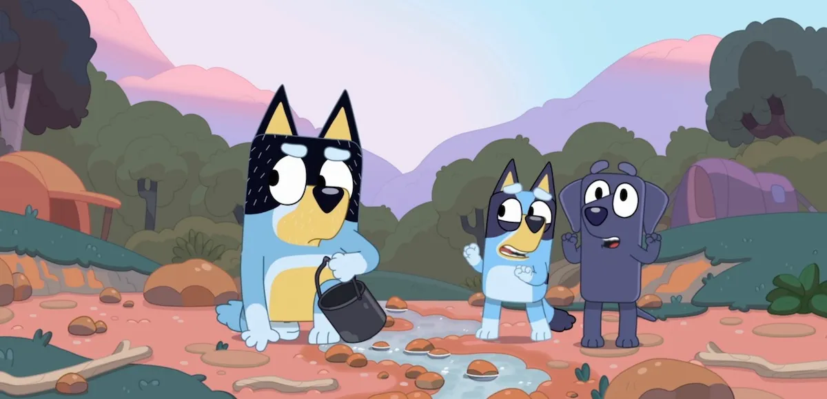 Bandit frowns while Bluey and Jean-Luc look on in a creekbed.