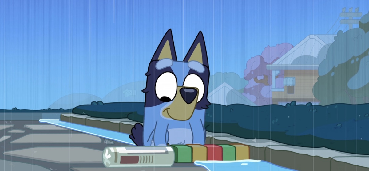 Blue sits in the rain, smiling down at some toys in front of her.