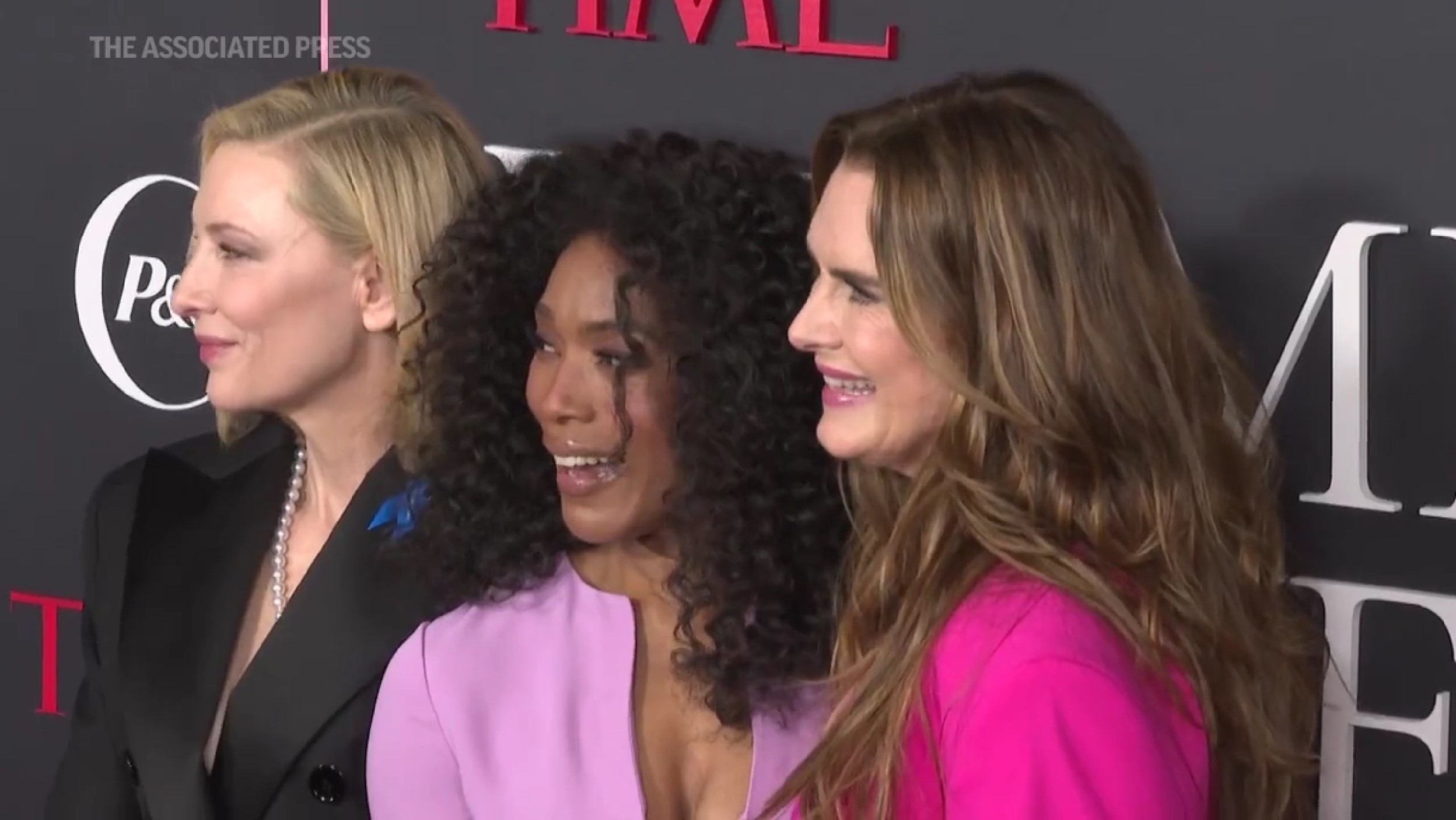 (left to right) Actors Cate Blanchett, Angela Bassett, and Brooke Shields standing together on the red carpet for the 'TIME Magazine' Women of the Year event. Cate is blonde and is wearing a black tuxedo jacket and pearls. Angela has shoulder-length curly Black hair and is wearing a purplish-pink suit with a low neckline. Brooke has long, brown hair, and is wearing a bright pink blazer. We see them all from the shoulders up, and they're all facing left and smiling.