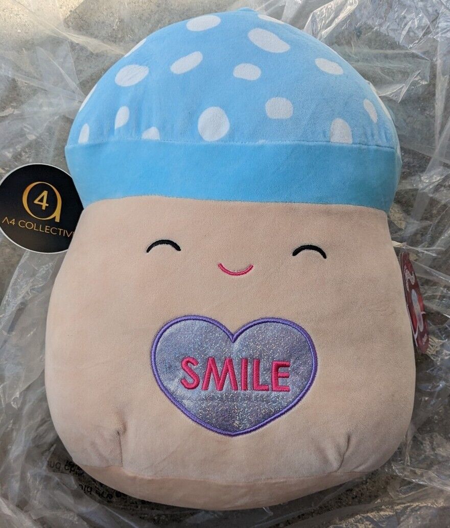 A mushroom Squishmallow with a white spotted blue cap and a blue heart saying smile on its stomach.