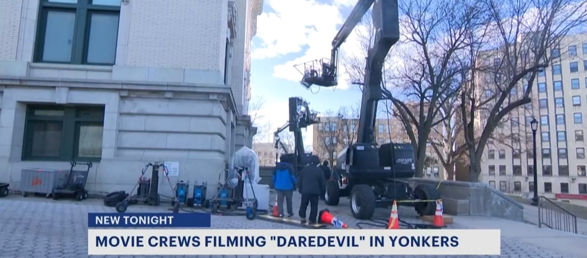 Cranes and film equipment set up outside a building. At the bottom is a banner saying "Movie crews filming Daredevil in Yonkers."