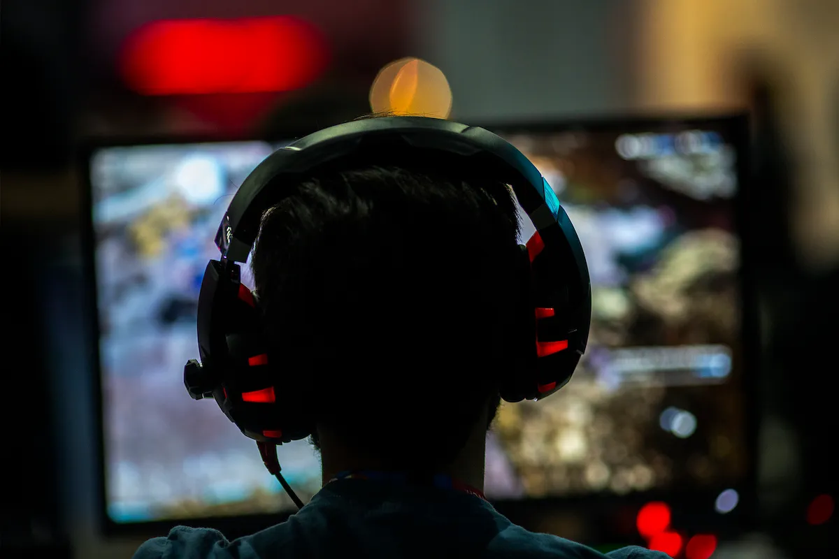A gamer seen in silhouette from behind, wearing large headphones, looking at a screen