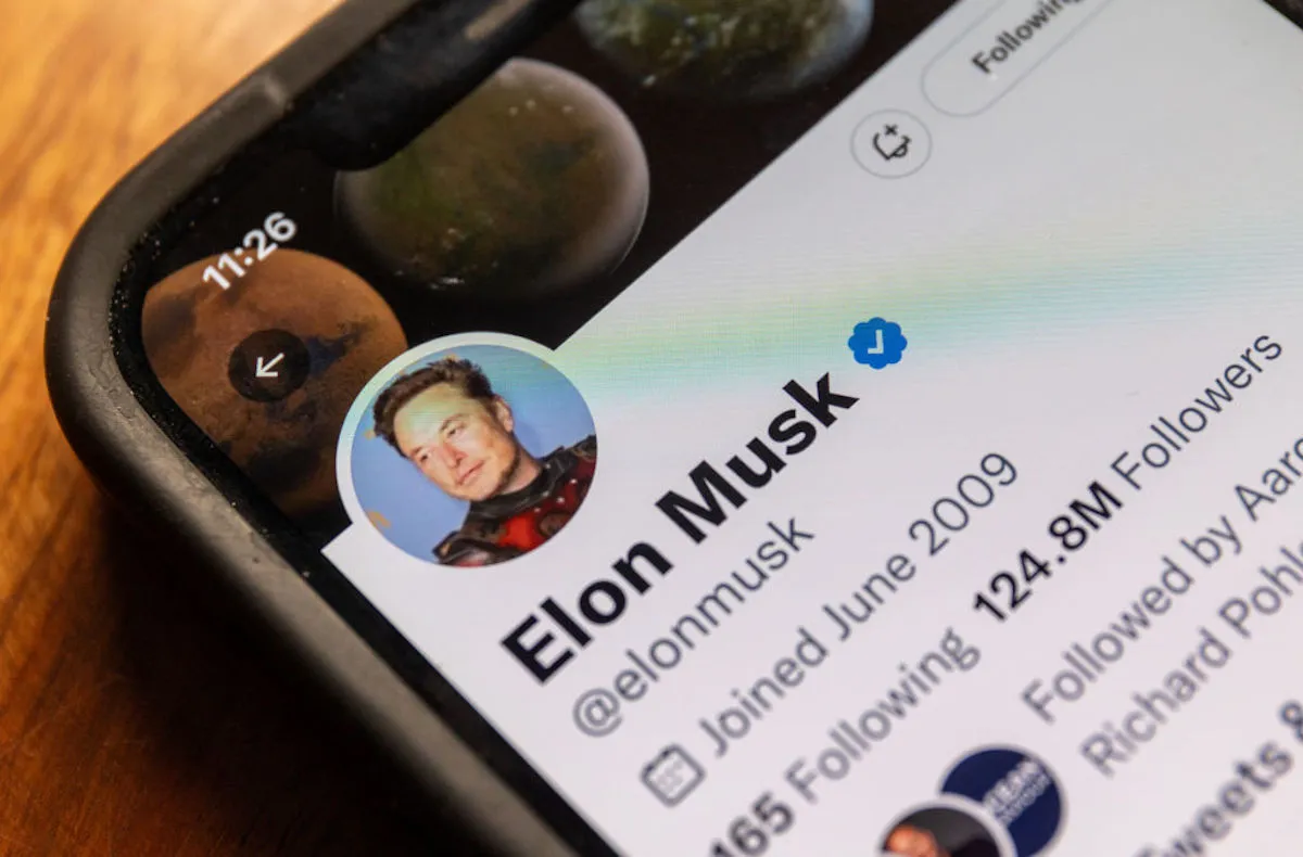 Corner of a phone with Elon Musk's Twitter profile visible on the screen.