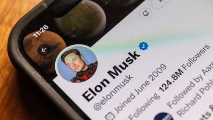 Corner of a phone with Elon Musk's Twitter profile visible on the screen.