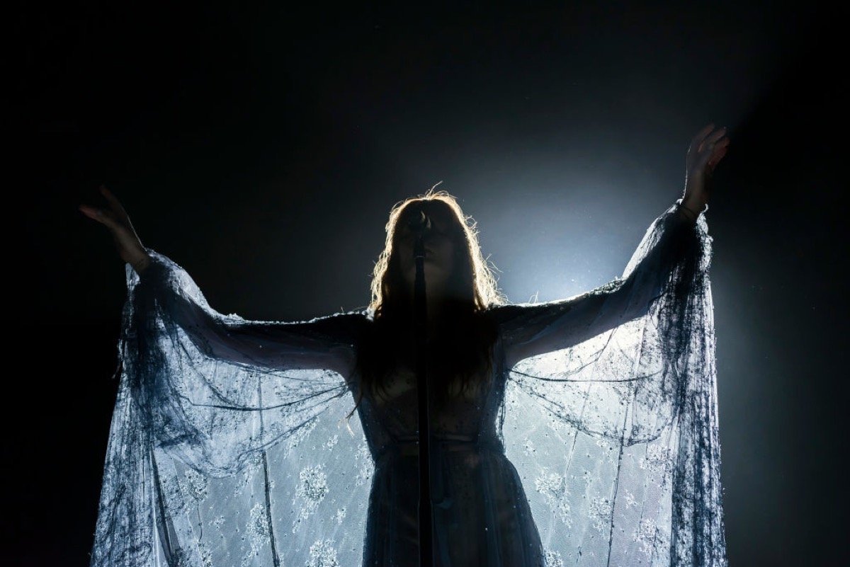 Florence Welch of Florence + The Machine performs at Rod Laver Arena. She's against a black background, in silhouette, strikingly lit from behind.