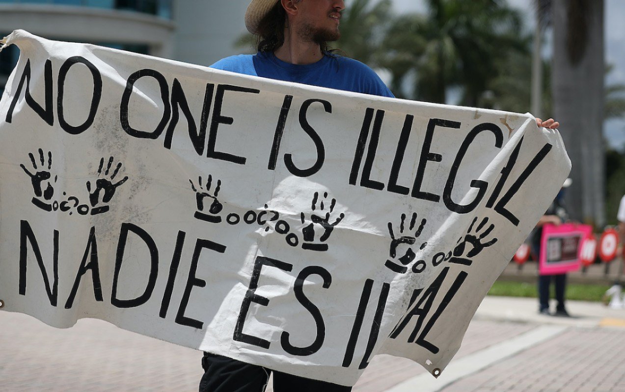 A protester holds a sign reading "No one is illegal"