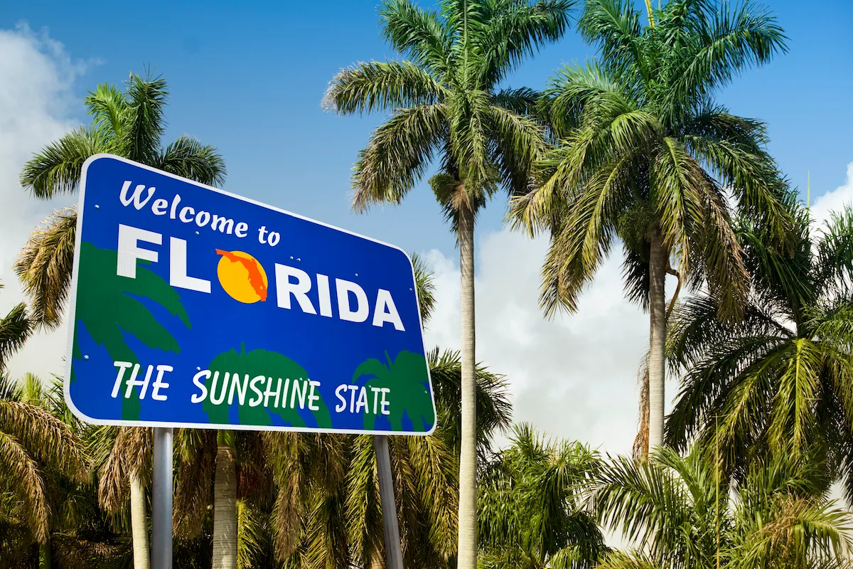 A road sign reading "welcome to Florida" with palm trees behind it.