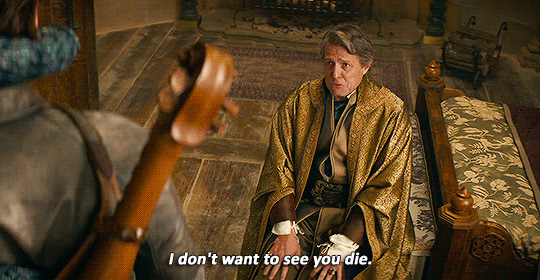 GIF of Hugh Grant as Forge and Chris Pine as Edgin in 'Dungeons & Dragons: Honor Among Thieves.' Forge is seated at the foot of a bed in an ornate bedroom wearing gold robes saying "I don't want to see you die" (which is text at the bottom of the GIF). We then see Edgin enveloped by a large, bluish tentacle. 