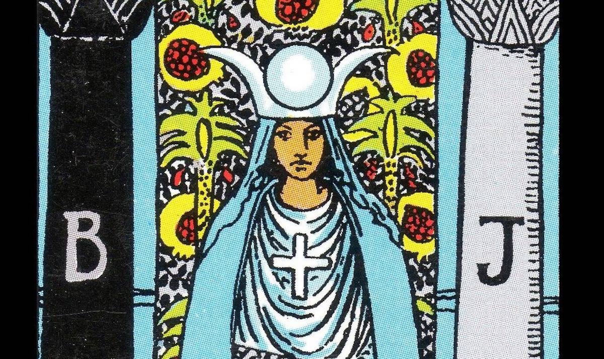 Detail from the High Priestess Card in the Smith-Waite Tarot. A woman sits between two pillars, with a large white headdress.