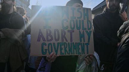 A woman at a protest holds a cardboard sign reading 