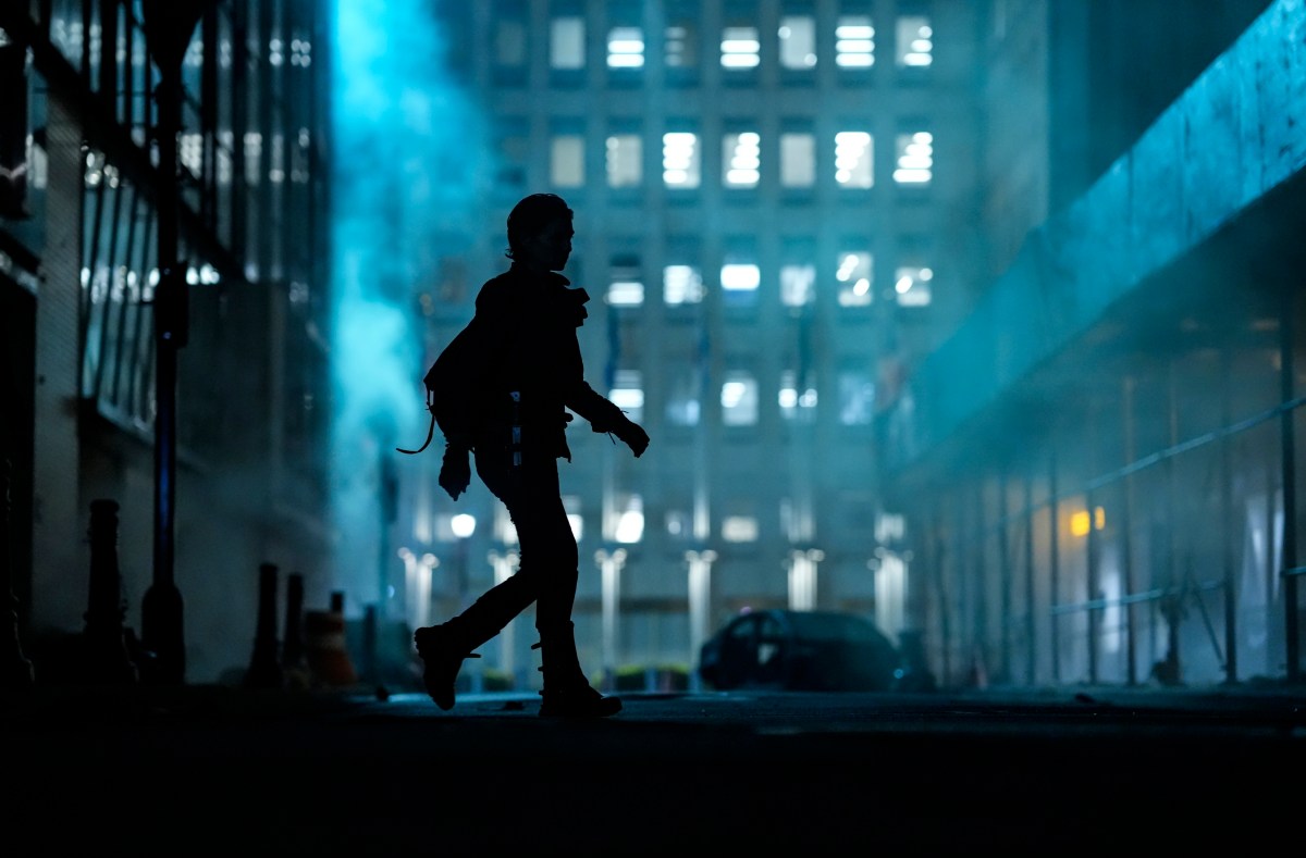 Lauren Cohan as Maggie in a scene from AMC's 'The Walking Dead: Dead City.' We only see Maggie in full-body silhouette as she walks across a street in downtown New York. She is illuminated by the bluish light coming from a still-functioning streetlamp at the end of the street in the distance.