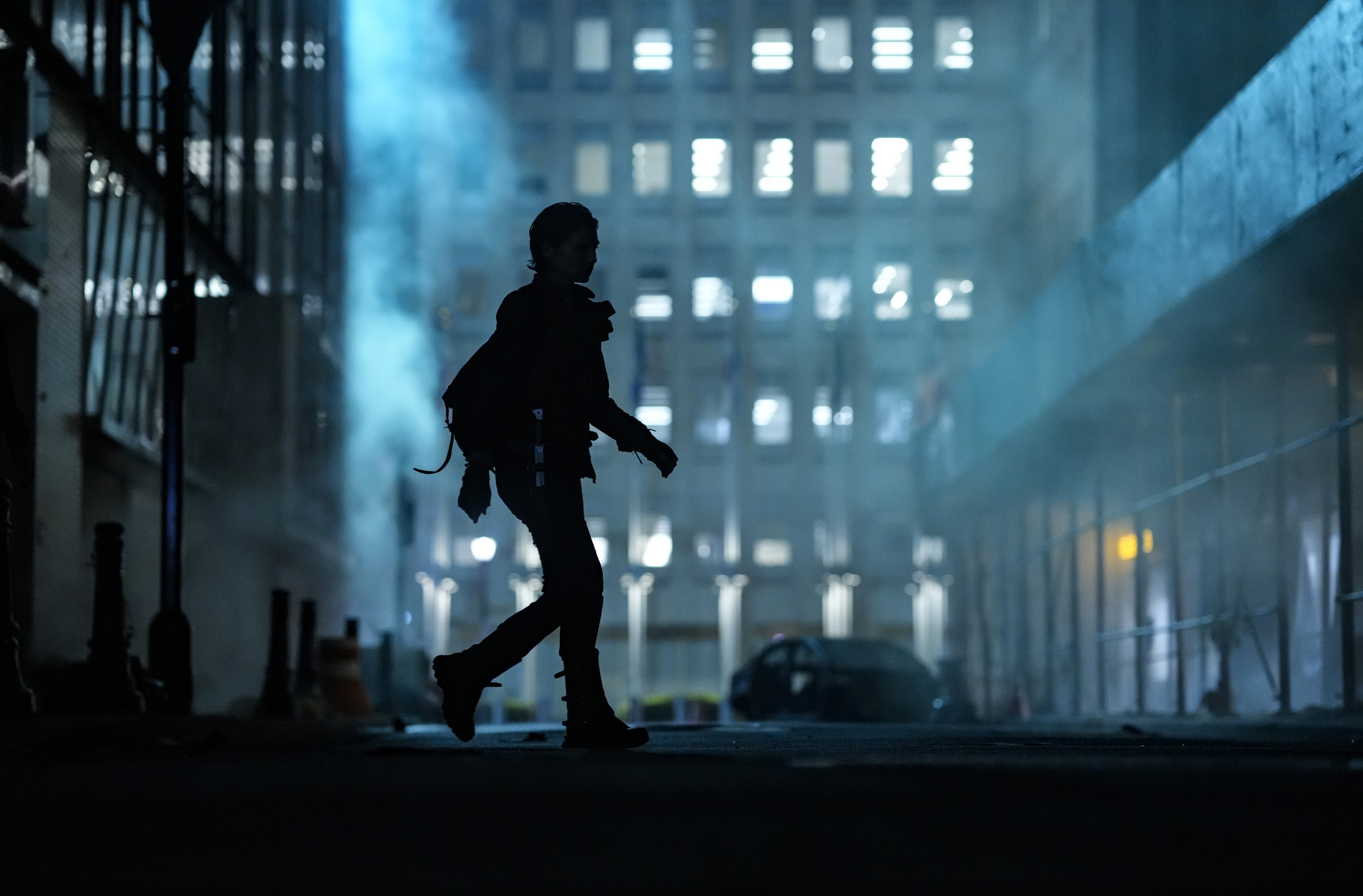Lauren Cohan as Maggie in a scene from AMC's 'The Walking Dead: Dead City.' We only see Maggie in full-body silhouette as she walks across a street in downtown New York. She is illuminated by the bluish light coming from a still-functioning streetlamp at the end of the street in the distance.