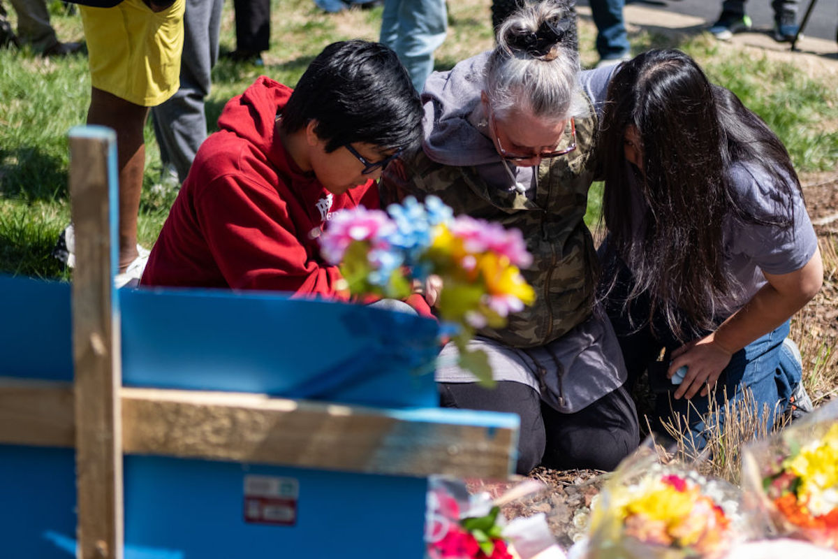 A group of people mourn at a memorial outside.
