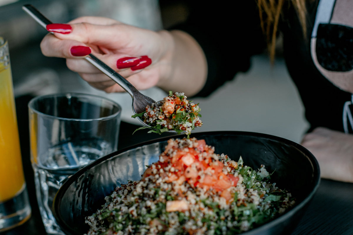 A woman with bright red finger nails holds a forkful of salad