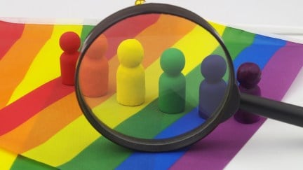 Many people figures rainbow colored on LGBT pride flag under magnifying glass isolated on white.