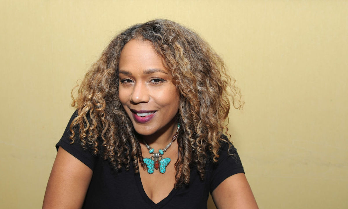 Rachel True smiles, wearing a black shirt and a turquoise butterfly necklace.