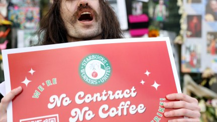 A protester with long hair and a mustache yells, holding a sign reading 
