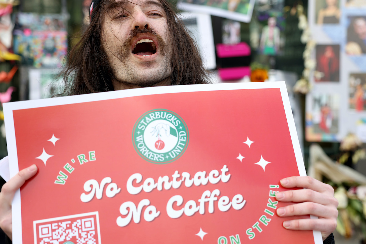 A protester with long hair and a mustache yells, holding a sign reading "No Contract, No Coffee"