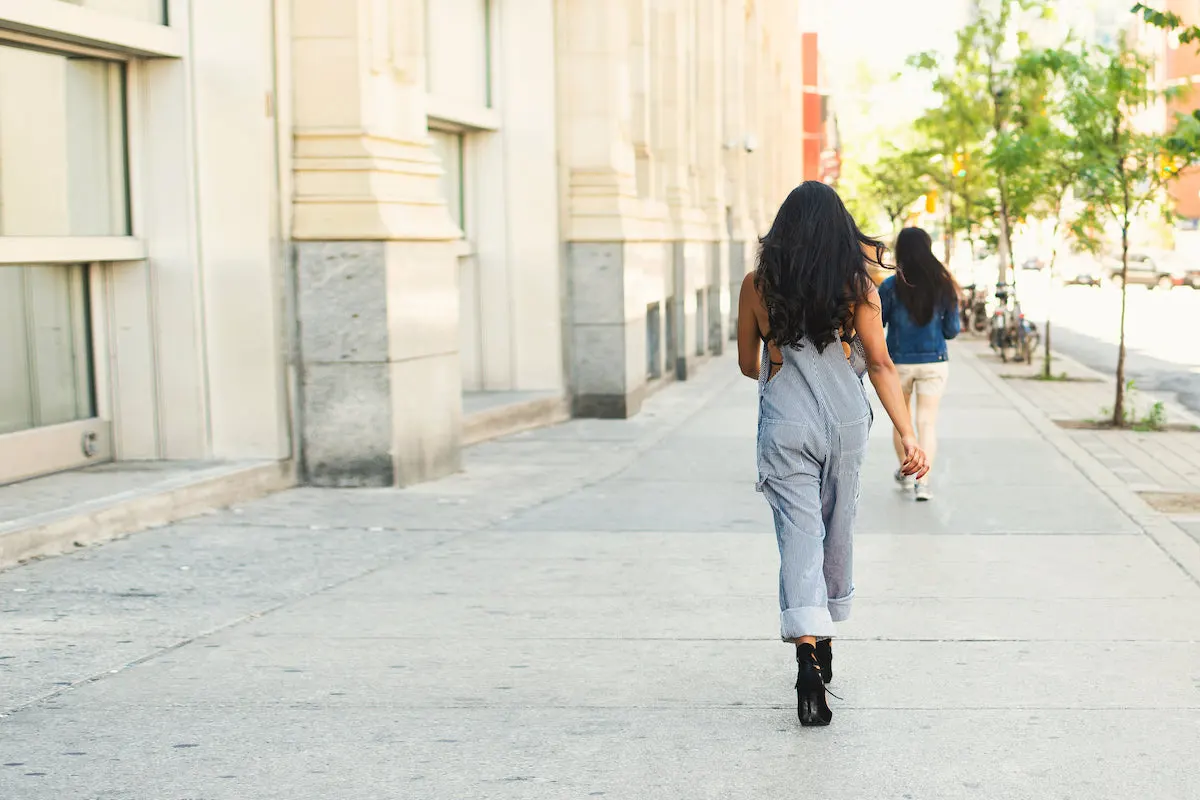 A woman walking along a wide urban sidwealk, seen from behind.