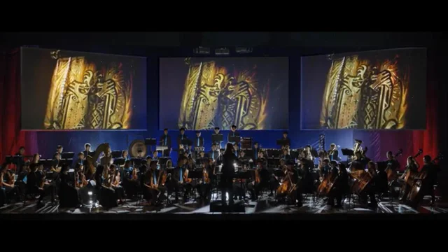 An orchestra with three screens behind it, showing a flag from Monster Hunter.
