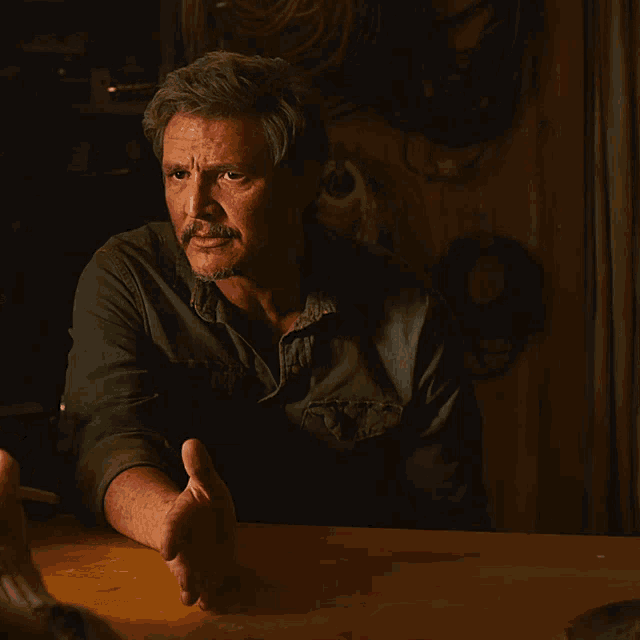 A GIF of Pedro Pascal as Joel in 'The Last of Us' on HBO. He's seated at a table talking to someone looking frustrated. He begrudgingly says "Okay."