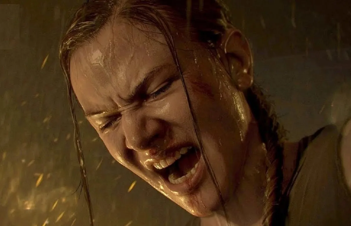 Close up of Abby's face in the last of us, part 2. Her mouth is open and her eyes squeezed shut as she screams in rage. It's raining and she's wet. Her blonde braid is hanging over one shoulder.