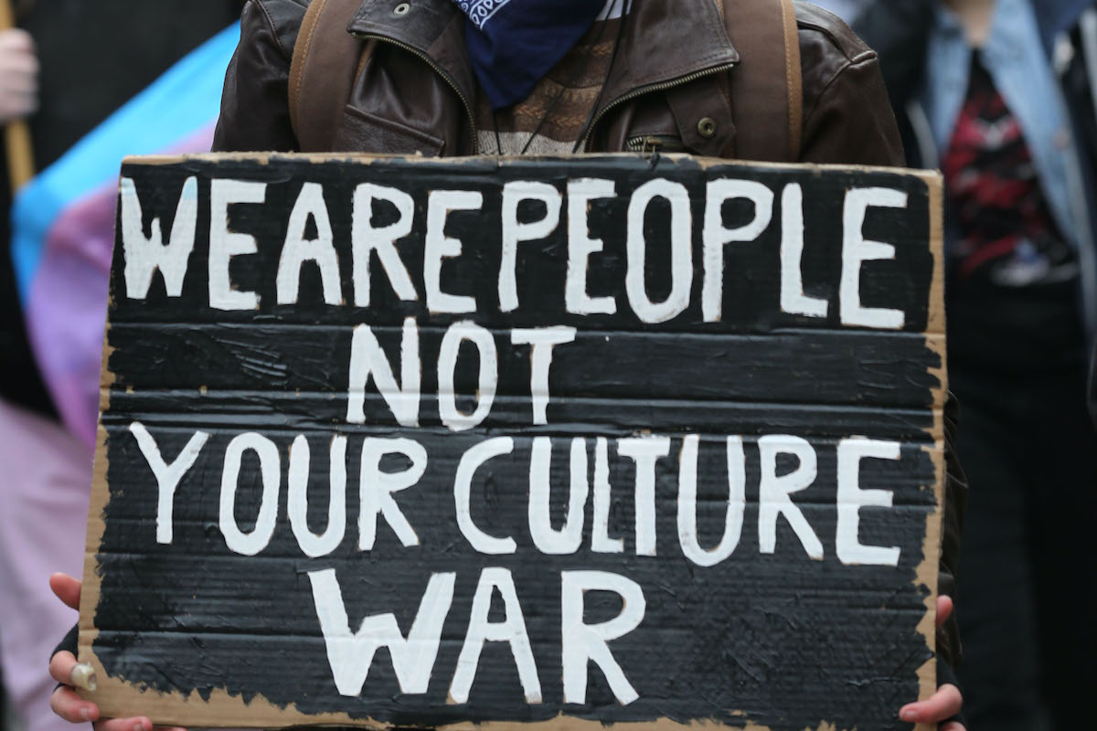 A cardboard protest sign reading "We are people not your culture war"