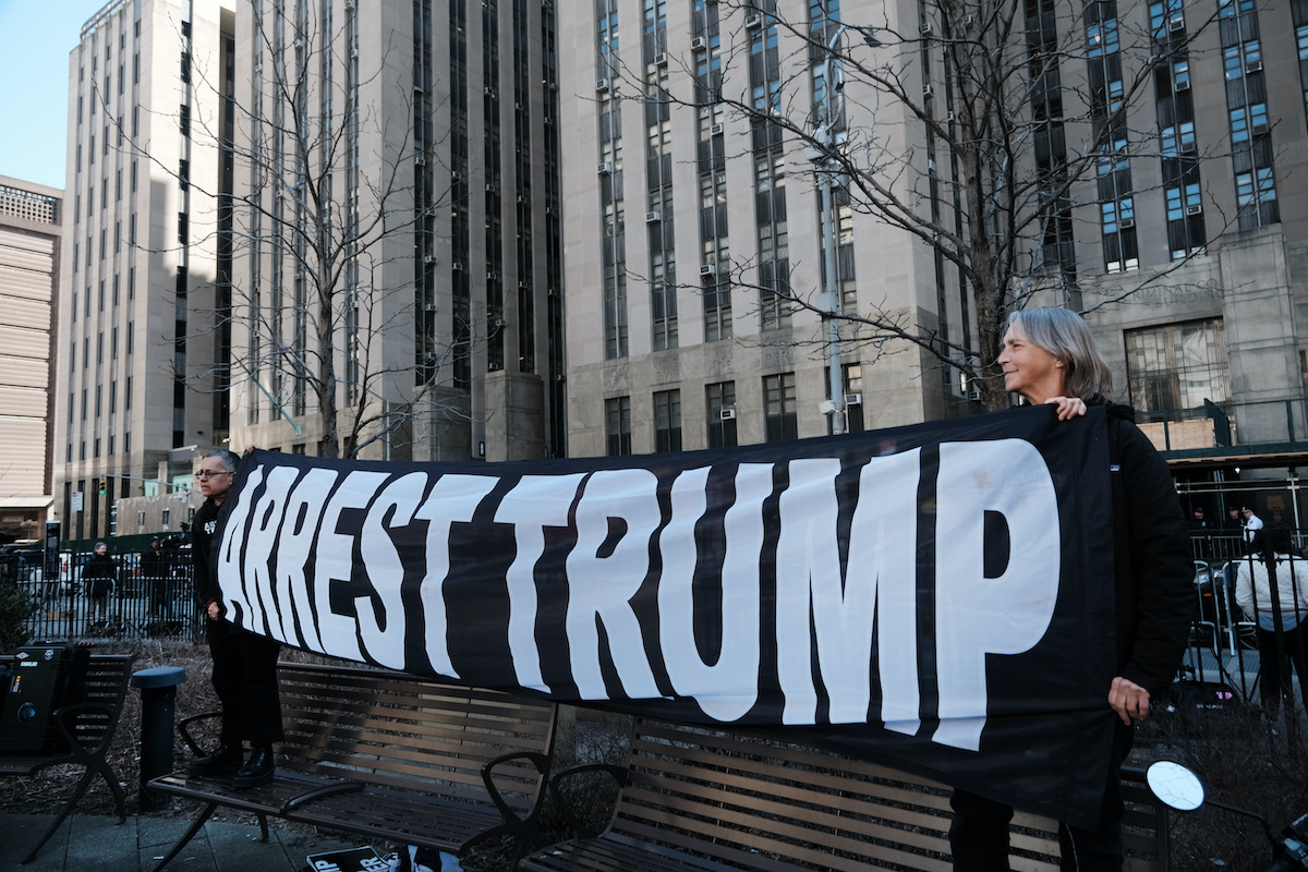 Protesters hold a large banner reading "arrest trump" on a New York City street.
