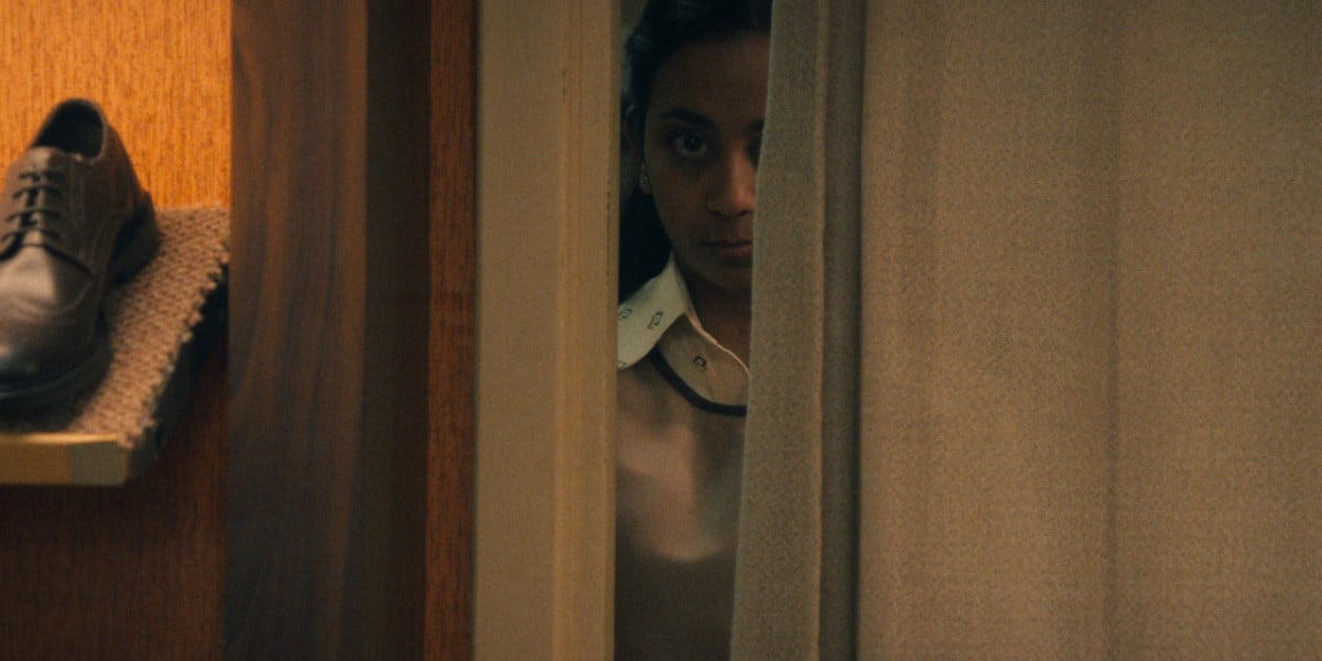 Anjana Vasan staring menacingly at something from behind a curtain Black Mirror season 6 promotional image