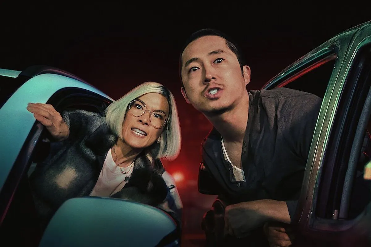 An Asian woman and man lean out the window of their respective cars with vengeful looks on their faces.