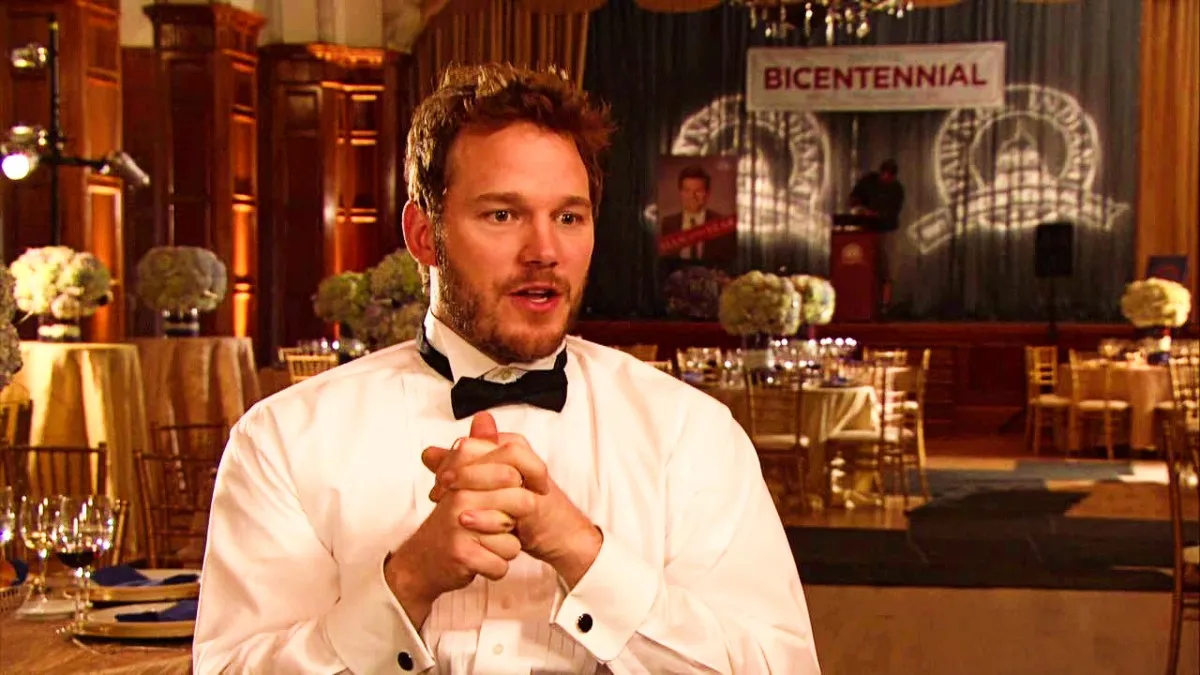 Chris Pratt as Andy Dwyer in "Parks and Recreation" sitting in a chair wearing a white shirt and a bowtie.