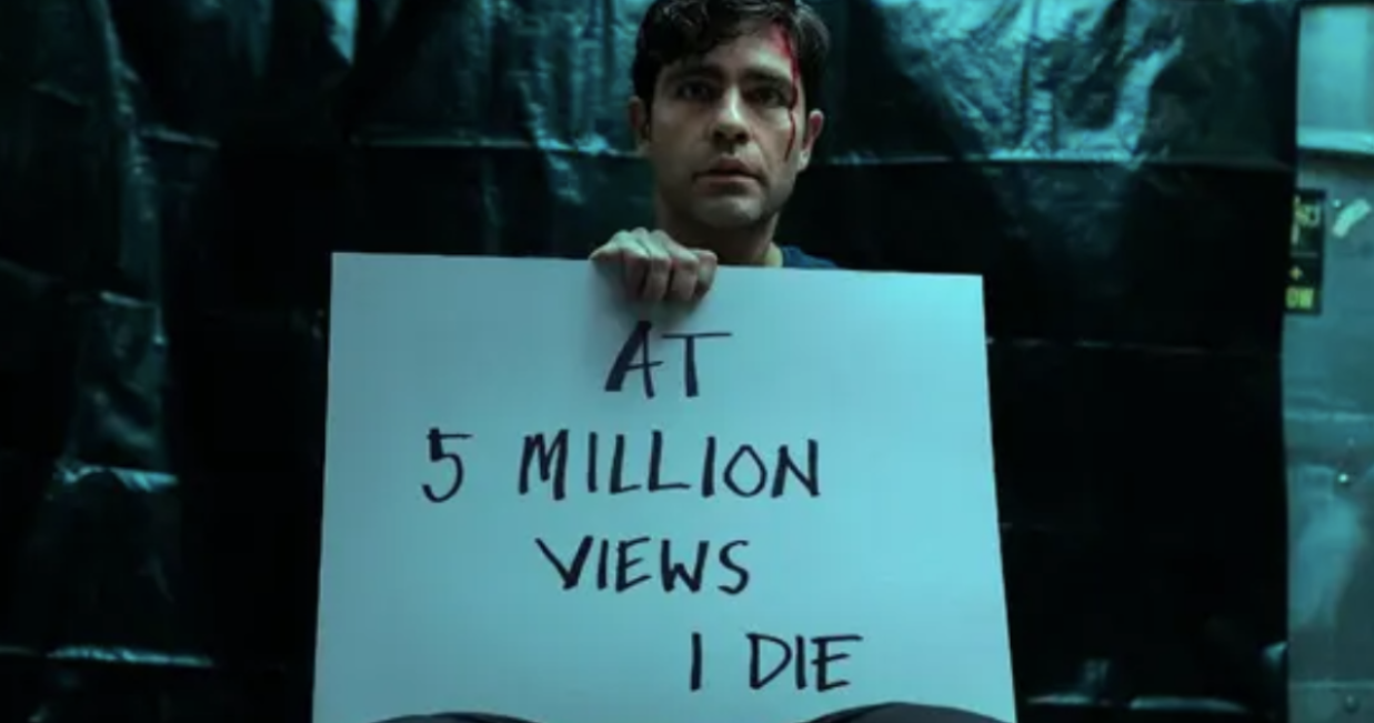 Nick Brewer holds a sign that says "At 5 Million Views I Die"