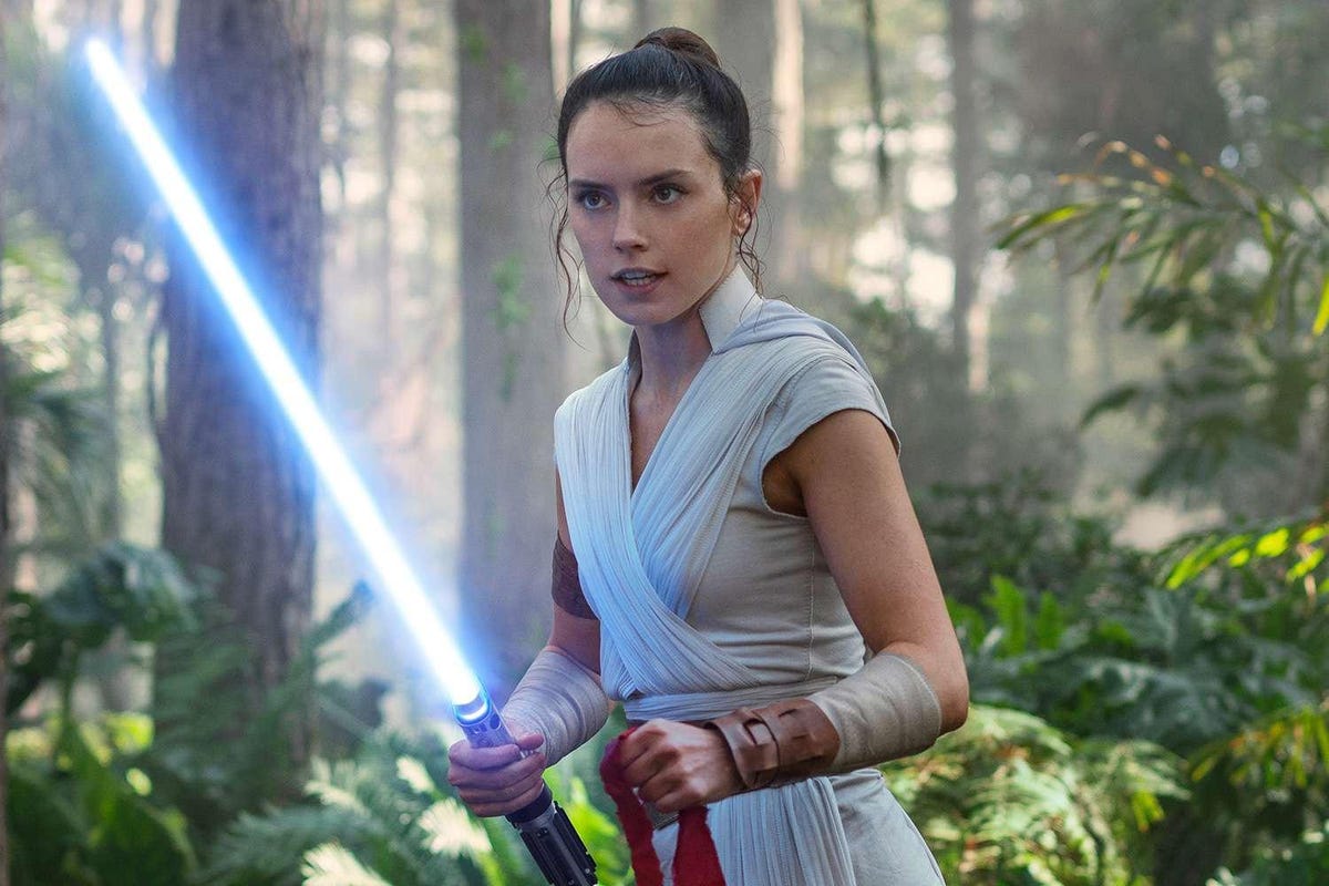 Daisy Ridley as Rey, wielding a lightsaber in a forest in 'Star Wars'