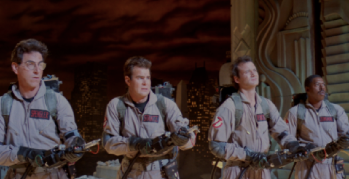 The four Ghostbusters stand in a line