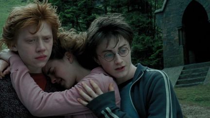 Ron Weasley, Hermione Granger, and Harry Potter stand in a group hug